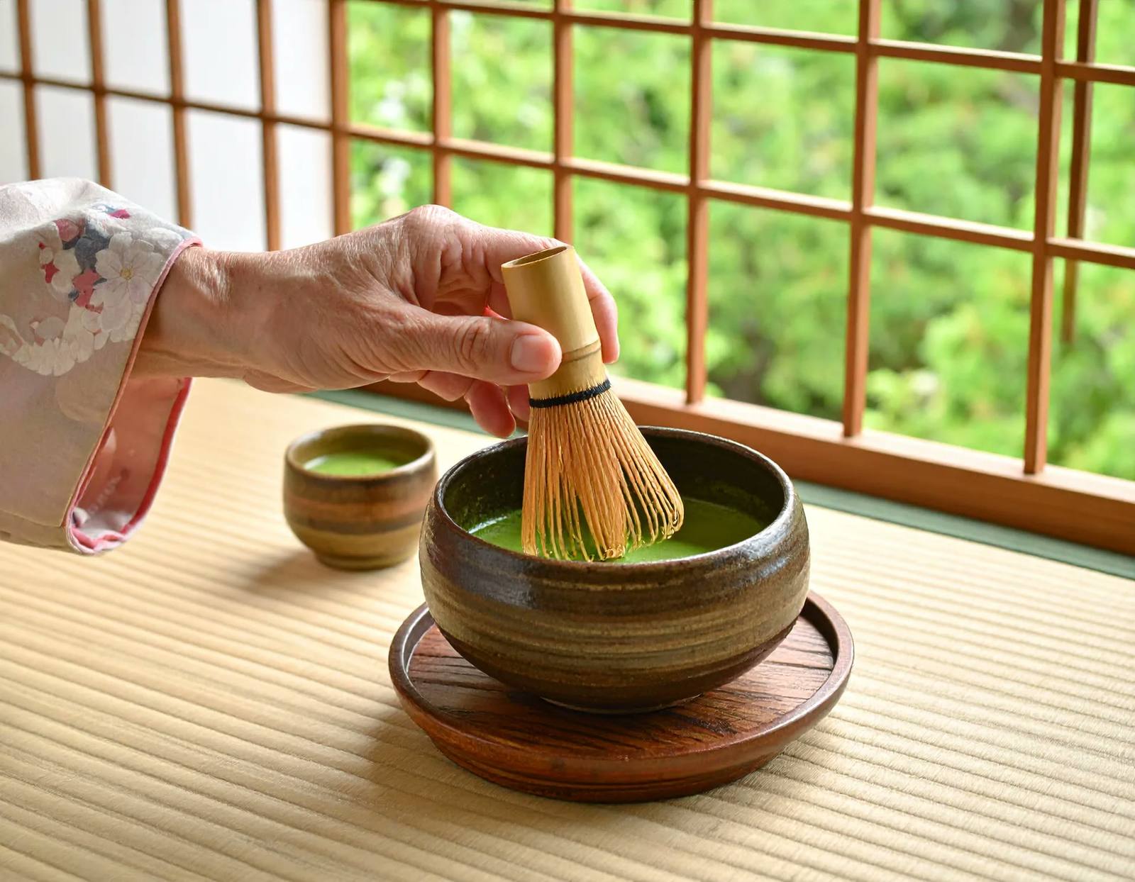 A hand whisking matcha with a bamboo chasen in a ceramic bowl